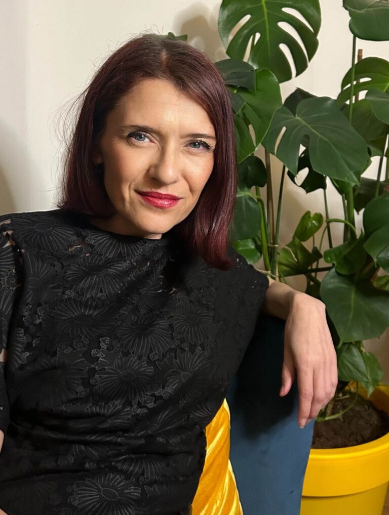 Sitting woman in a black blouse with short, auburn hair.