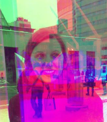 A woman's reflection in a window overlaid against a city street backdrop.